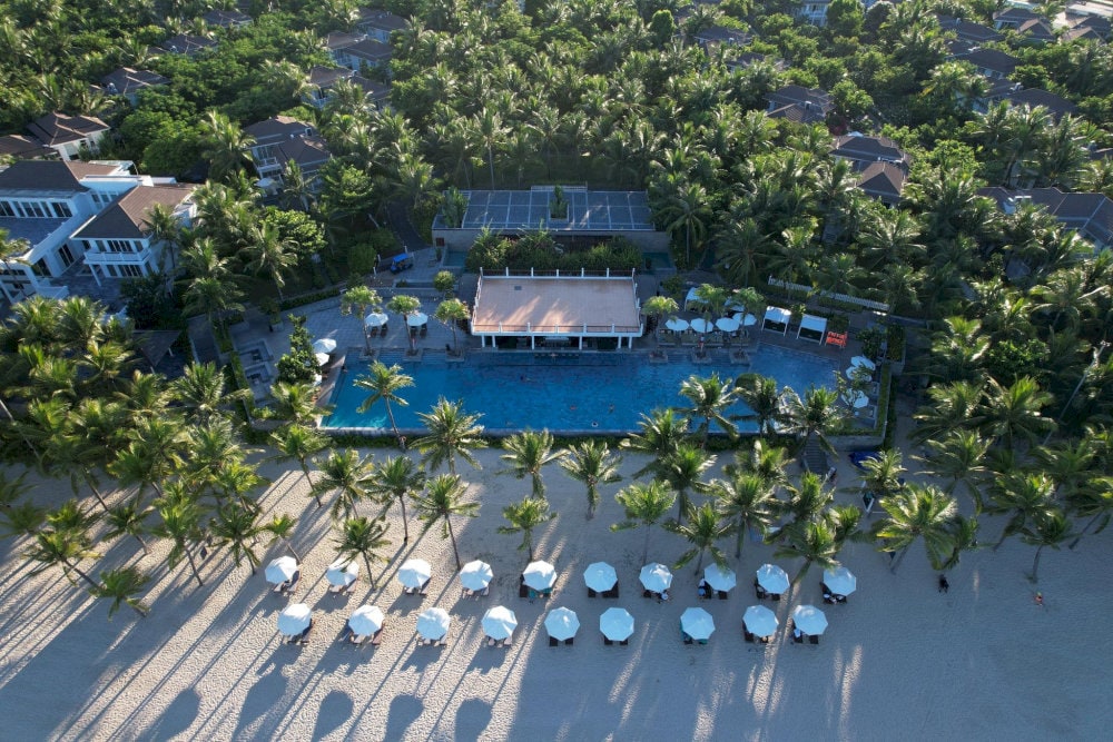An organized beachfront setting featuring a central pool, shaded lounges, and seamless coastal views